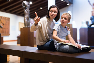 Attentive boy with young tutor looking at exposition in historical museum, pointing to something