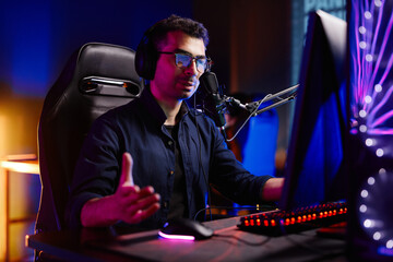 Portrait of streamer playing video games in dark studio with neon accents and speaking to microphone