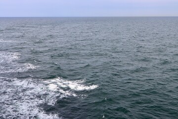Stern waves with white foam tips on greyish blue sea water, photo taken from aboard ship. Selective focus