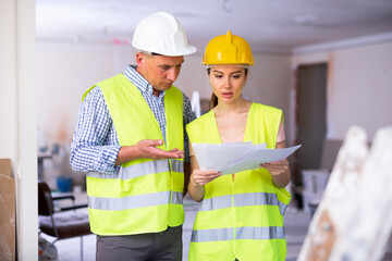 Male and female builders having conversation about work plan in apartment. Discussing documentation details.