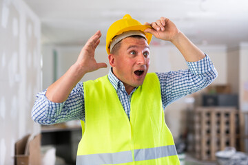 Frustrated worker in yellow vest and hard hat is dissatisfied with the way the walls are plastered