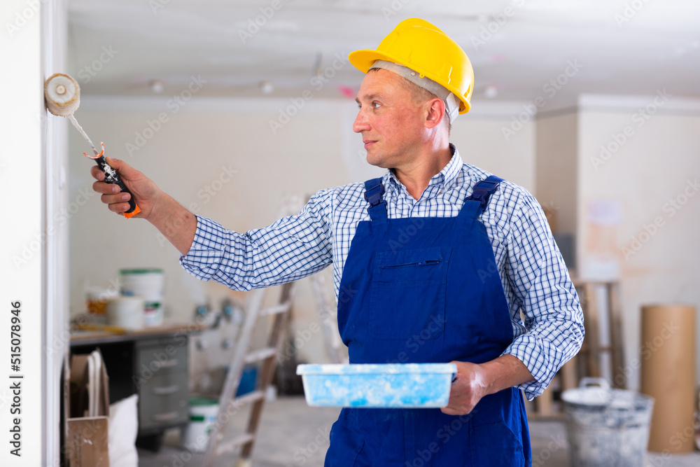 Wall mural painter painting wall in apartment with roller, home improvement works.