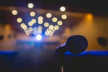 Closeup of microphone on stage of a big entertainment room with spotlight and blurry lights