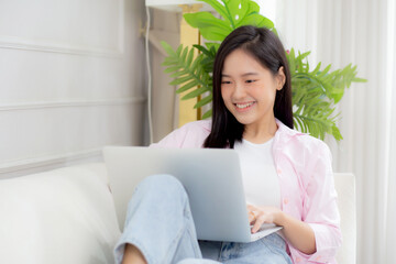 Obraz na płótnie Canvas Young asian business woman work from home with laptop computer online to internet on sofa in living room, freelance girl using notebook sitting on couch with comfort and relax, lifestyles concept.