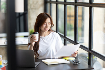 Serious beautiful young woman typing on laptop in a bright modern office, Charming asian businesswoman sitting working on laptop in office.