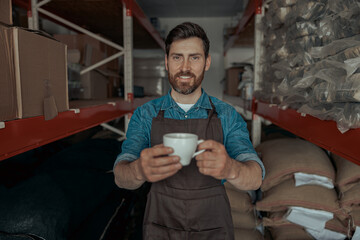 Barista propose to you cup of fresh coffee on the background warehouse of coffee factory