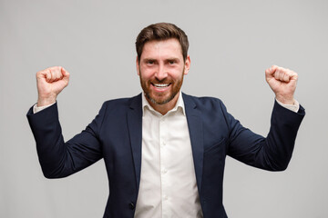 Happy joyful businessman wearing suit doing winner gesture clenching fists 