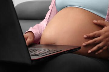 pregnant woman working on laptop sitting on couch in living room