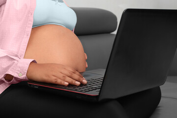 Latina pregnant woman using laptop on legs sitting on couch