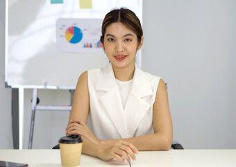 Asian businesswoman in white dress looking at camera, recording self-presentation video or sharing professional skills. Happy young smart people filming educational lecture.