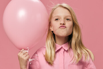 funny, happy, beautiful girl of school age, blonde, stands in a pink shirt with an inflatable pink ball in her hand and makes a funny face