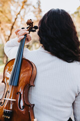 curly brunette woman holding a violin on her back, walking through the park road at sunset. Vertical