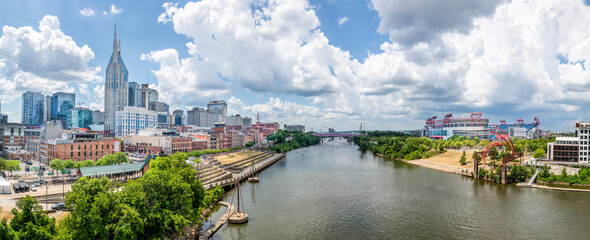 The Cumberland River flows through the city of Nashville, Tennessee, with downtown skyscrapers rising on one bank and a professional football stadium on the other. - obrazy, fototapety, plakaty