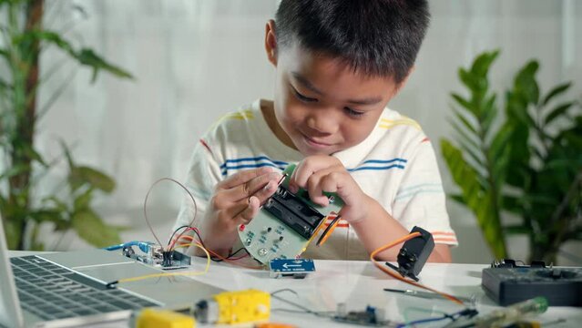 Little child trying assemble build wheel to car toy, Asian kid boy assembling wheel into Arduino robot car homework, creating electronic AI technology workshop online school lesson