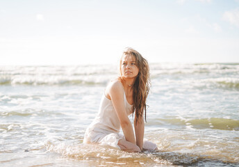 Fototapeta na wymiar Young blonde beautiful woman with long hair in white dress enjoying life on sea beach