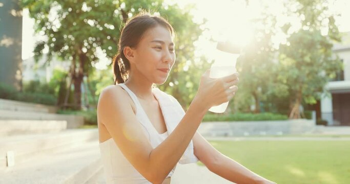 Beautiful young Asia athlete lady exercises drinking water because feel tired after running in urban park environment in evening. Outside workout and fitness healthy lifestyle concept.
