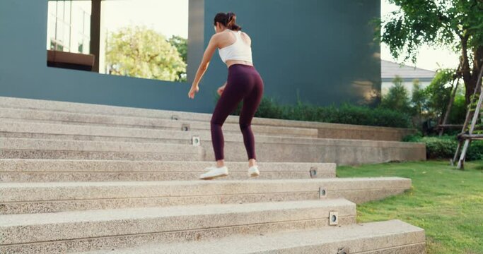 Beautiful young Asia athlete lady exercises doing squat jumps after running on urban stairs at park environment in evening sunset. Outside workout and fitness healthy lifestyle concept.
