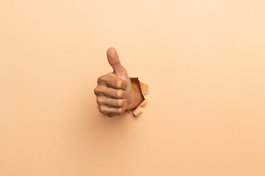 Close-up of male hand showing thumbs up on a brown background..