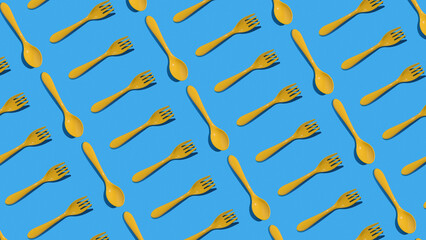 A pattern of yellow plastic forks and spoons on a blue background. Minimal concept of kitchen...