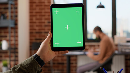 Company employee holding digital tablet with greenscreen in startup office, using isolated copyspace with mockup background and blank chroma key. Looking at digital web app on device.