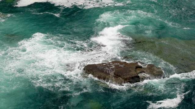 Powerful, unpredictable waves crash violently over rocks in the middle of the deep, teal coloured ocean while seabirds fly around the internationally important seabird colony on Handa Island, Scotland