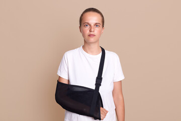 Indoor shot of Arm broken Caucasian woman with arm sling supported on her hand, being injured by...