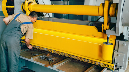 Worker cuts metal sheets on mechanical guillotine machine in production hall. Industrial equipment...
