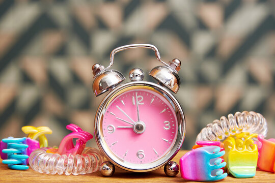 Pink fancy alarm clock with girly hairpins on the bed table. Teenage girls accessories backgrounds
