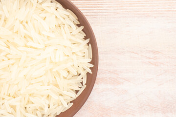 Long Basmati rice in clay plate with copy space on brown wooden background. Macro. Flat lay. Indian cuisine concept
