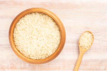 Long Basmati rice in wooden bowl and spoon on brown wooden background. Flat lay. Healthy eating concept