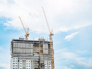 Two construction cranes are working on the construction of tall buildings, lifting and placing things. The construction site is covered with blankets. in the clear sky city building in a straight line