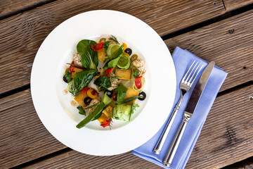 Tasty tuna salad with lettuce, black olives, eggs and fresh vegetables on wooden table