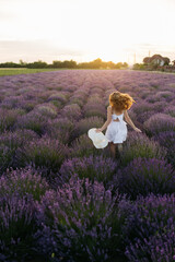 Provence, France. A girl in white dress walking through lavender fields at sunset.