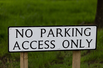 White road sign with the words No parking, access only in front of a green background