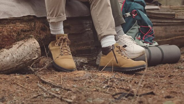 Low section slowmo of two unrecognizable people sitting on log in forest, hiking or camping