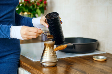Closeup view of hand with spoon with ground coffee near a turk