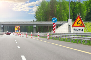 Roadworks, large bright mobile sign with stripes, detour direction and flashing yellow arrow on road service truck trailer in right lane on highway.