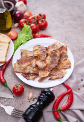 fried bacon pieces in a plate and vegetables at domestic kitchen stone or concrete table