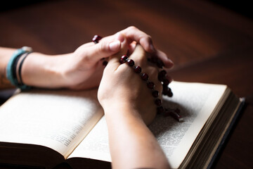Obraz premium Christianity theme – prayer. Christian woman with Bible praying with hands crossed keeping rosary.