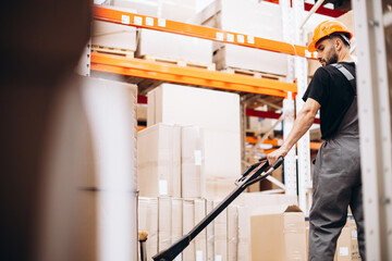 Workman at the factory pulling pallet jack with cardboard boxes