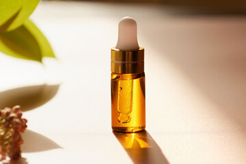 Cosmetic amber glass dropper bottle with oil, serum or fruit peeling in the sunlight on beige...