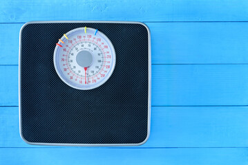 Naklejka premium Mechanical weight scale, body mass control concept : Bathroom scale on pale blue wood background. Analog scale operated with spring that pressure is calibrated to translate tension into a mass readout