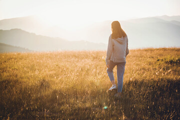 Young Girl in Hoodie Walking in Mountain Golden Field Landscape