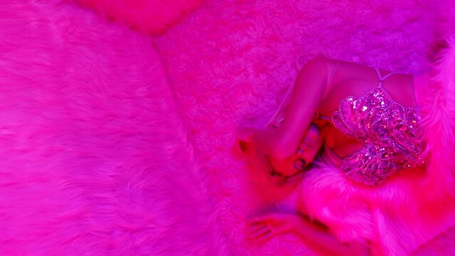 a gorgeous blonde is lying on the floor in furs with neon pink color and moves seductively