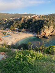 View from the top of a small bay with blue water between the lushy hills and rocks with cityscape in Kas, Antalya, Turkey