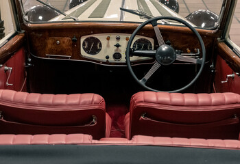 Monaco, April 2022. Image with the interior of a vintage car, very nicely maintained, with red painted leather seats and large steering wheel on the wooden dashboard.