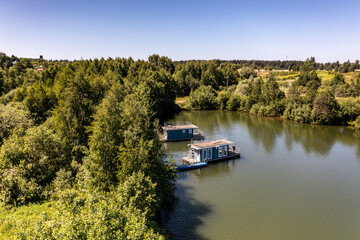 a panoramic view of the green forest and the lake and the glampings standing on the shore on a sunny summer day taken from a drone