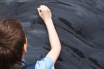 Boy standing back in front of school blackboard and writing