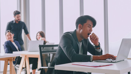 A young company employee is feeling tired while sitting at work for a long time.