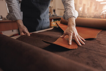 Tailor cobbler hold different rolls natural brown leather, working with textile in workshop